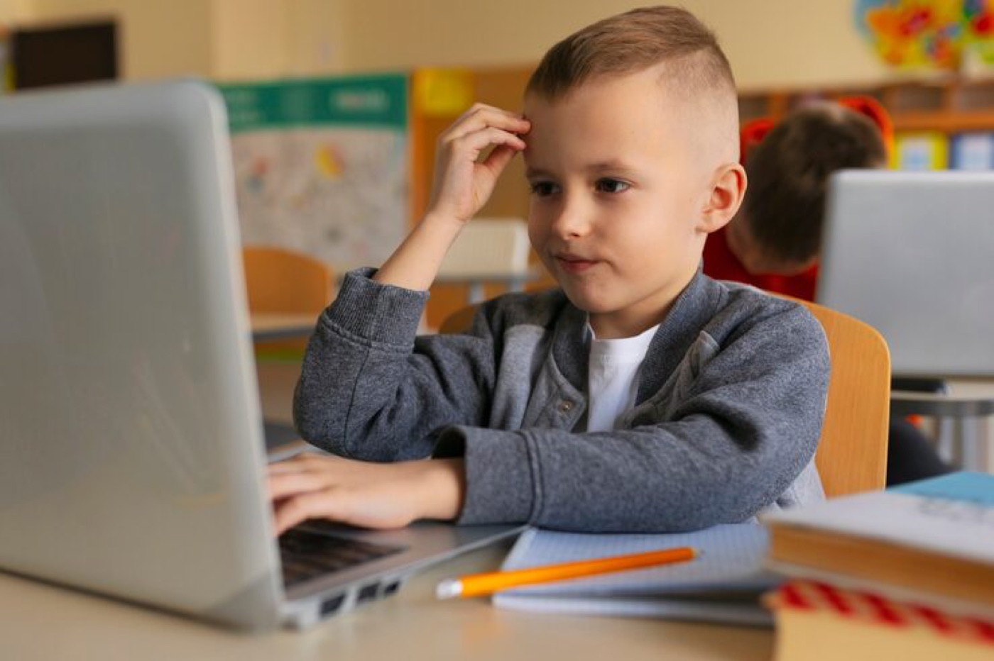 Un niño pensando frente a su portátil en clase